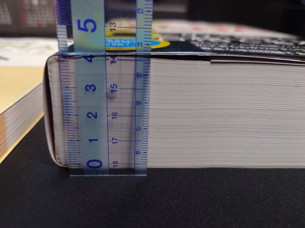 定規を当てて、CCNA学習書の厚さを横から測っている写真。分厚いテキストのボリューム感が分かる。