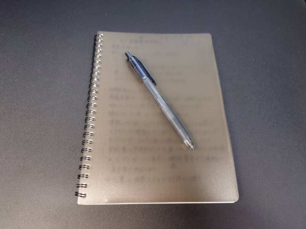 今使っているA5サイズのリングメモ帳とボールペンを机の上に置いた写真。仕事の中でメモを取る習慣を支えている愛用品。